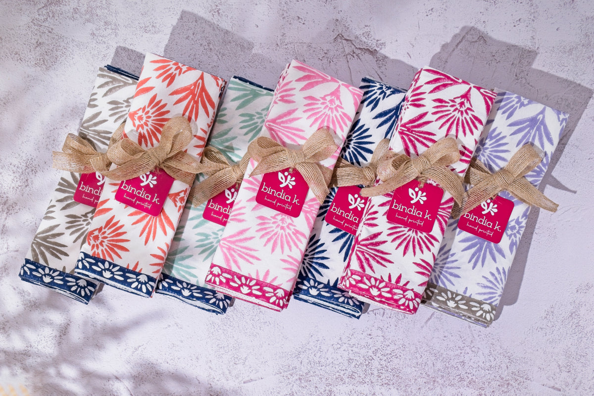 Set of folded cotton napkins with floral patterns and brand labels on a textured surface